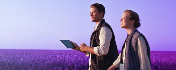 A man and a woman walking together in an open field, surrounded by grass and natural scenery